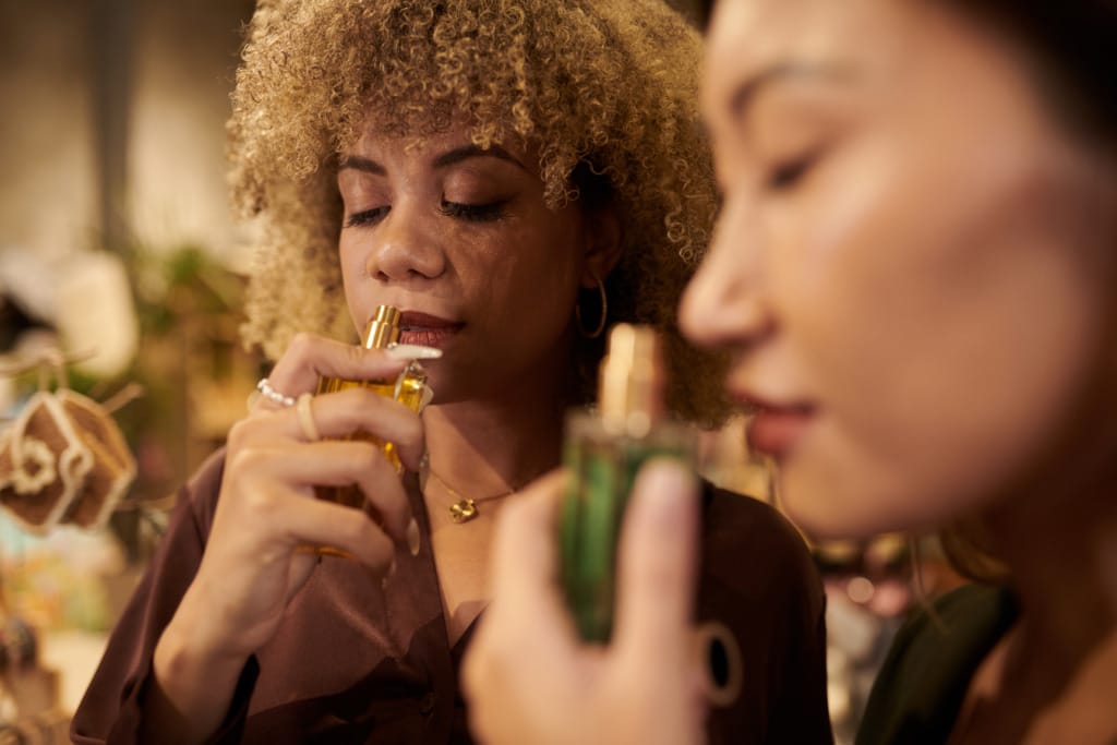 A close up of 2 glamorous women with their eyes closed, holding luxurious perfume bottles as if pondering "What perfumes do celebrities wear?"